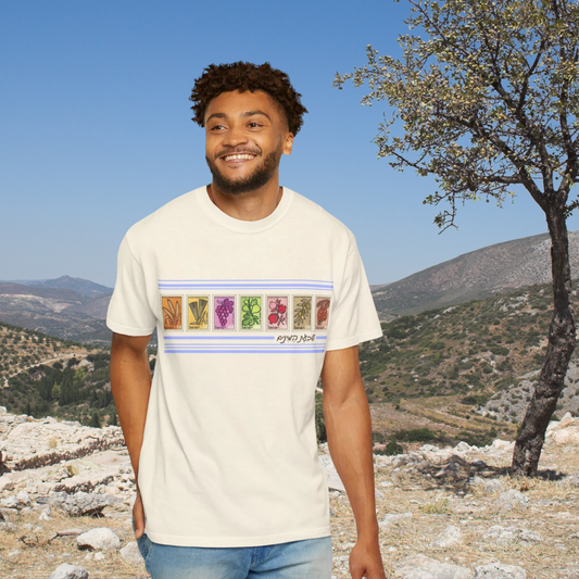 Man wearing a white t-shirt with colorful graphics and text, standing outdoors with mountains and trees in the background.